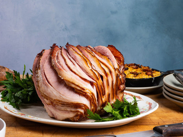 A sliced spiral ham with a golden-brown glazed exterior, served on a white plate with parsley garnish, set on a wooden table with a blue textured background.